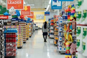 A woman walking away down the aisle of a supermarket.